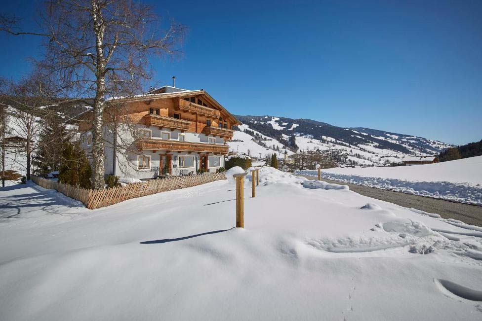 Außenansicht der Pension Enzian im Winter mit verschneiter Landschaft und alpiner Bergkulisse.