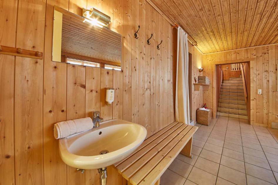 Heller Wellness-Umkleidebereich mit Holzvertäfelung, Waschbecken, Sitzbank und Zugang zum Ruhe- und Saunabereich in der Pension Enzian.