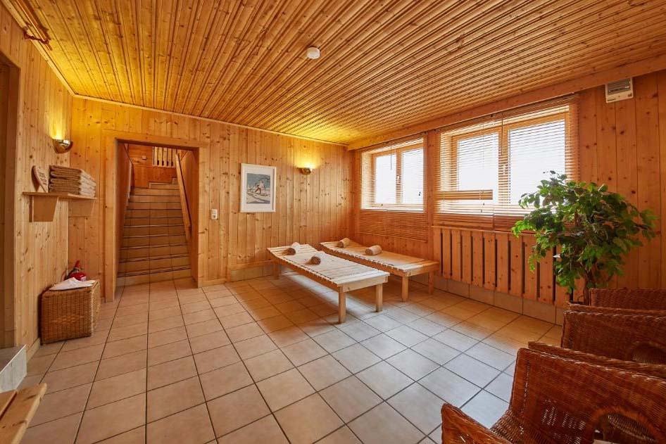 Großzügiger Wellness-Ruheraum mit Holzliegen, Tageslicht und alpinem Ambiente in der Pension Enzian.