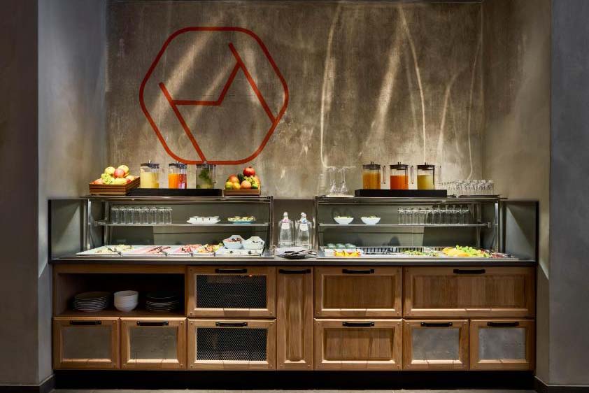 The Modernist Hotel-Frühstücksbuffet mit Holzfront, Glasvitrinen, frischem Obst, Säften und minimalistischem Wanddesign in stilvoller Atmosphäre.