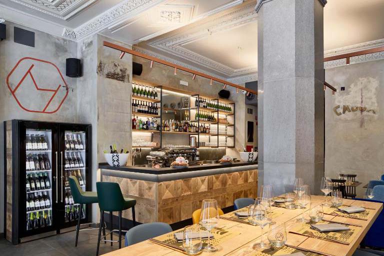 Eleganter Hotel-Bar- und Restaurantbereich mit gedecktem Holztisch, Barhockern, Weinregalen und urbanem Interior-Design im The Modernist Hotel.