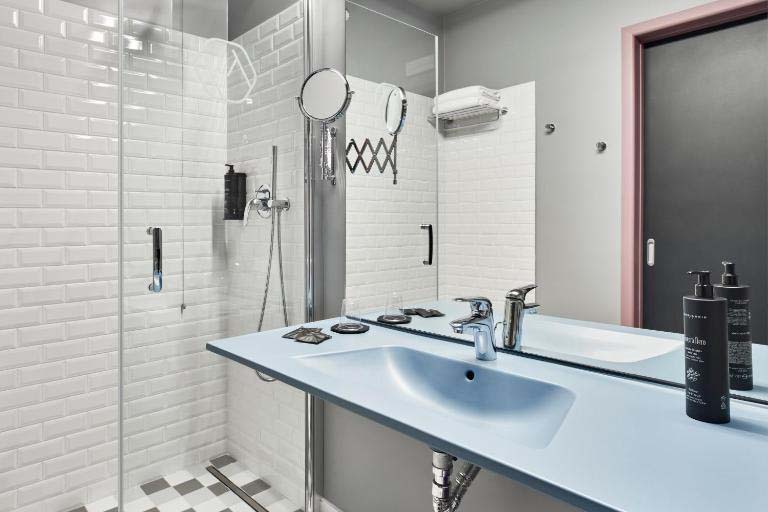 Badezimmer mit begehbarer Dusche, großem Spiegel, Waschbecken und hellem, funktionalem Design für komfortable Nutzung im The Modernist Hotel.