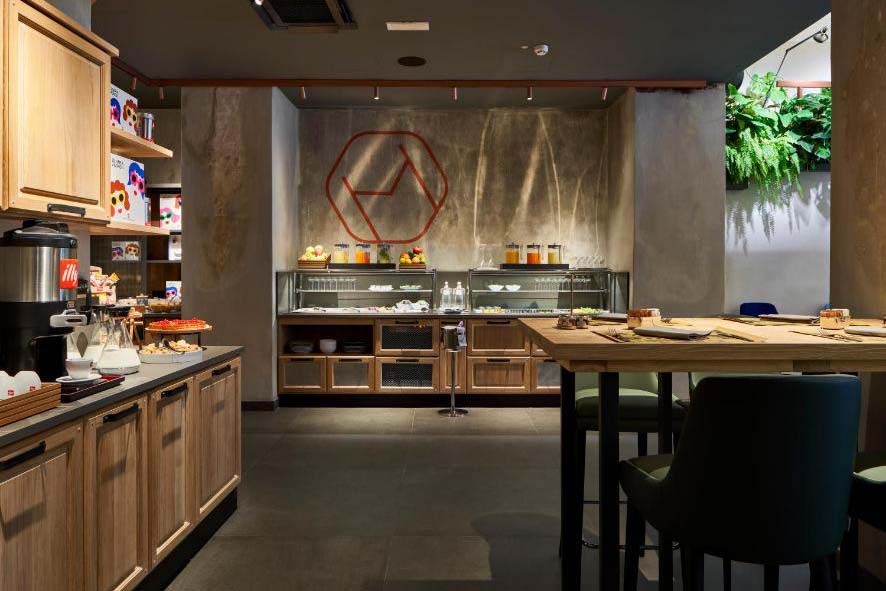 Großzügiger Hotel-Frühstücksraum mit Buffet, Holzmöbeln, Sitzbereich und modernem Design in warmen Naturtönen.