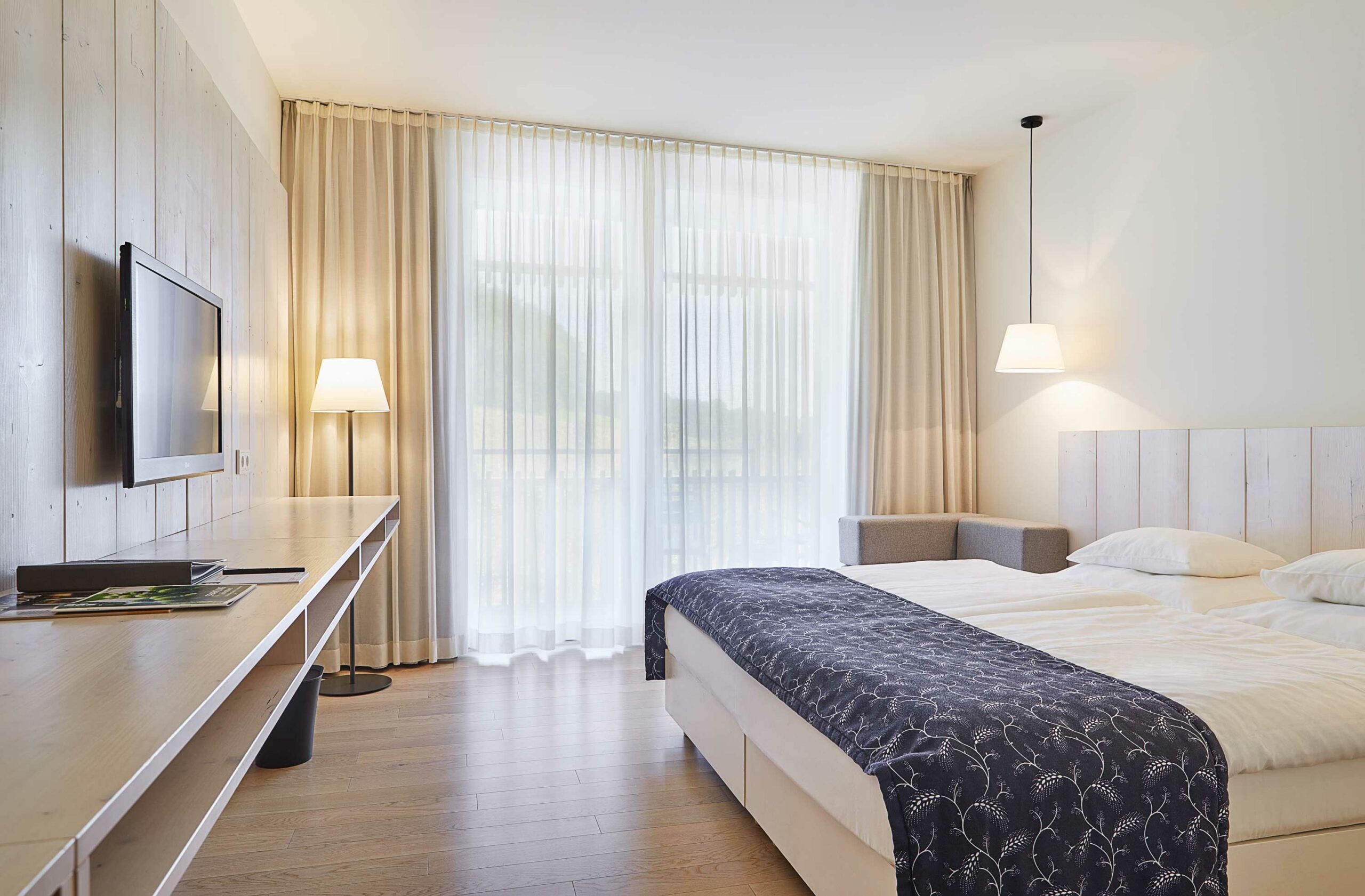 Modernes Doppelzimmer im LOISIUM Wine & Spa Hotel Südsteiermark mit Balkon, bodentiefen Vorhängen und Blick in die Weinlandschaft.