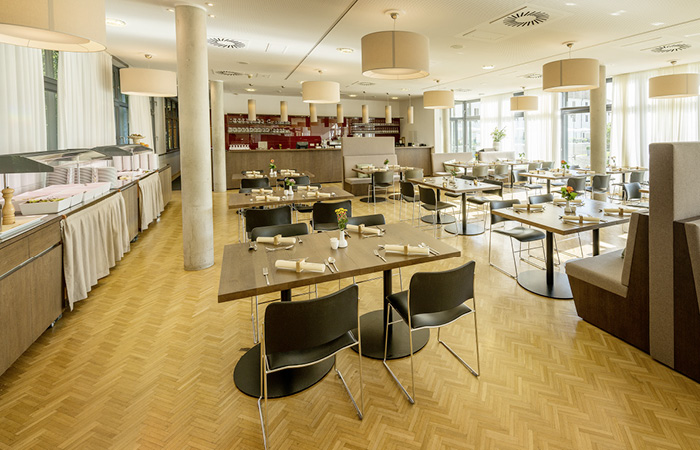 Moderner, heller Speisesaal mit Holzboden, mehreren gedeckten Tischen und großen Fenstern