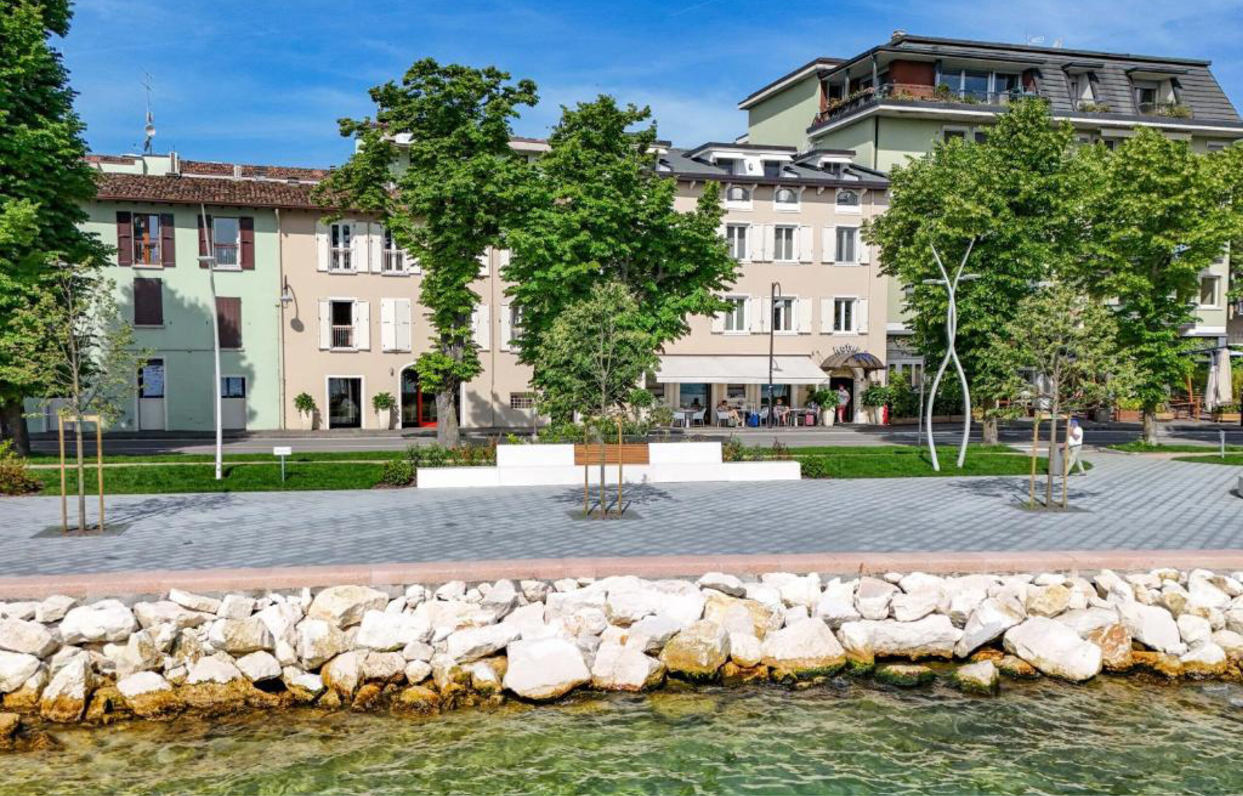 Uferpromenade mit Steinmauer, Bäumen und Sitzbänken vor mehrstöckigen Wohngebäuden