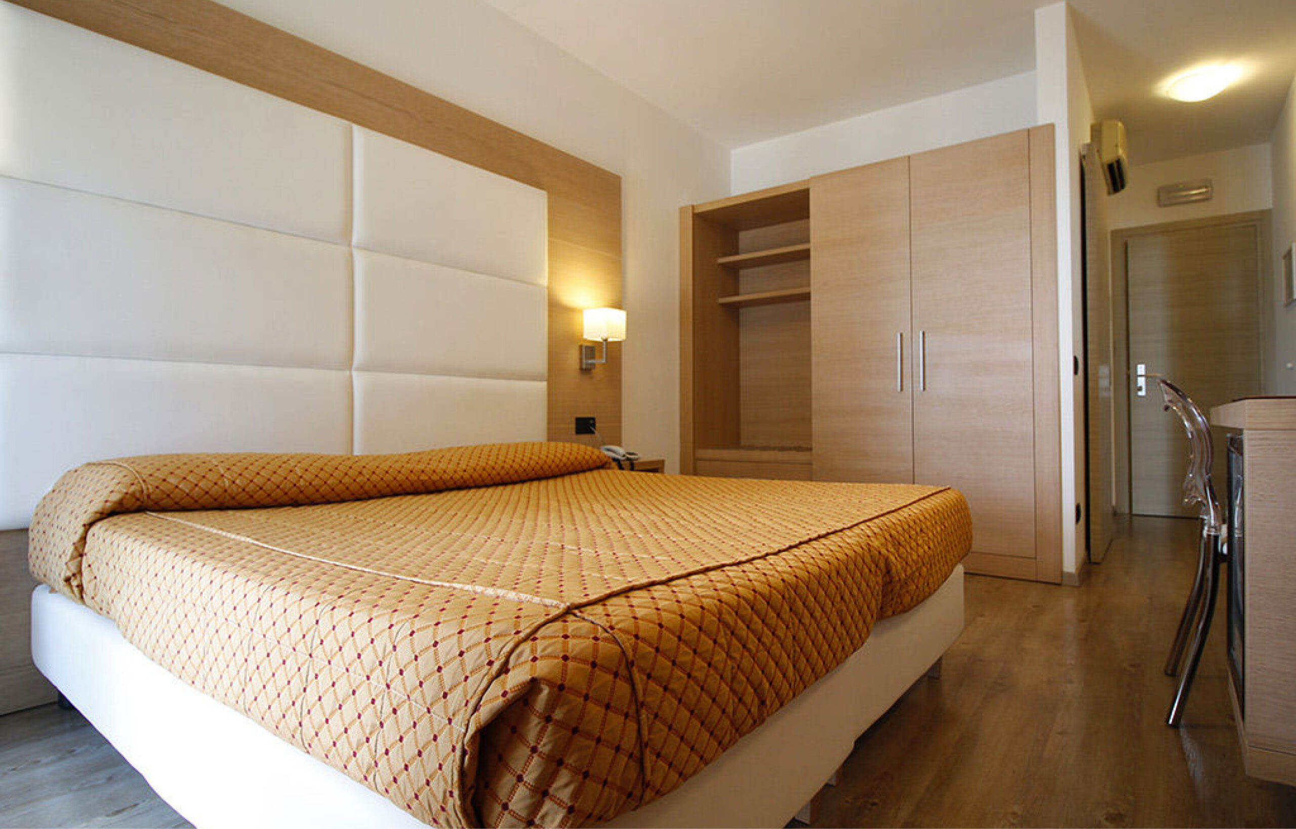 Hotelzimmer mit Doppelbett, gepolstertem Kopfteil, Holzmöbeln und Schreibtisch mit Stuhl
