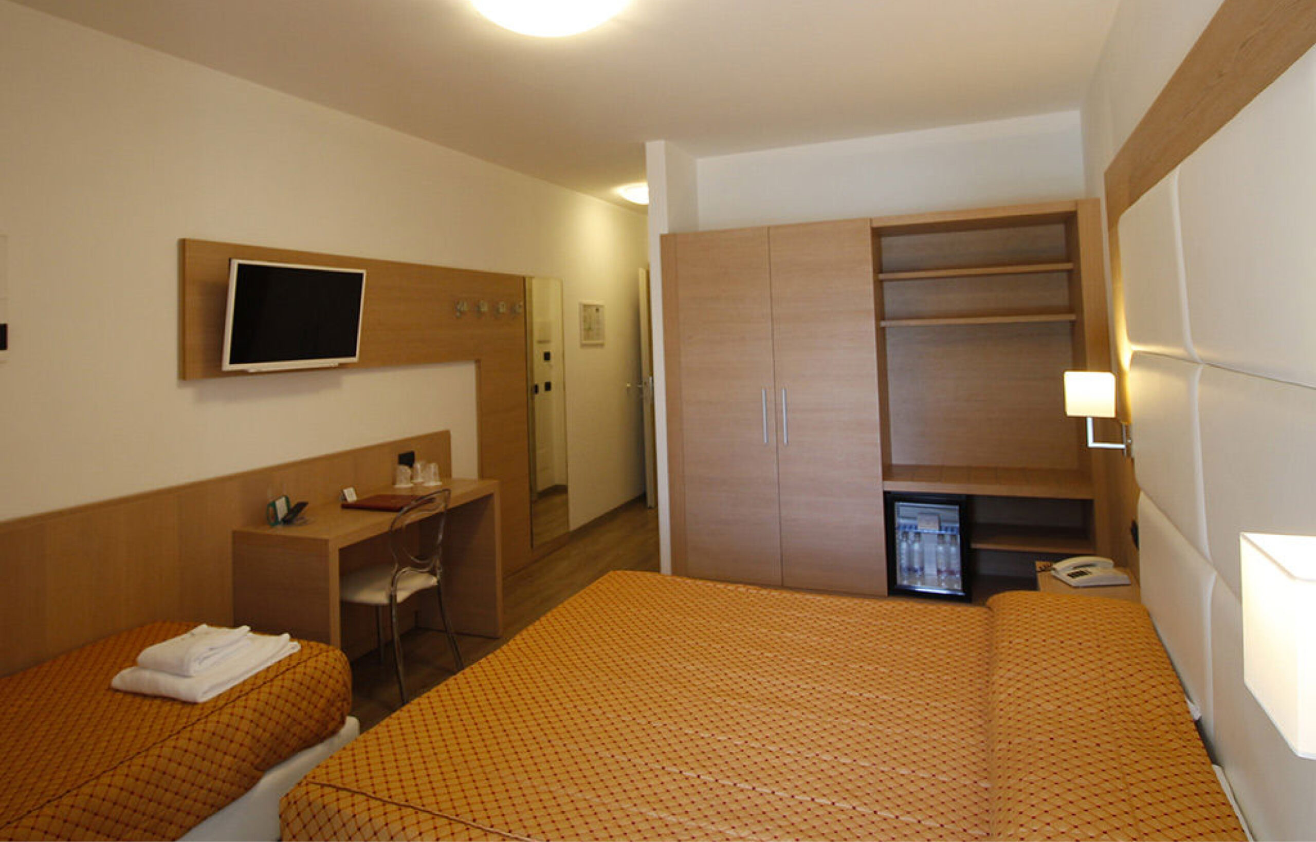 Hotelzimmer mit Doppelbett und Einzelbett, Wandfernseher, Schreibtisch, Kleiderschrank mit Minibar und warmen Decken