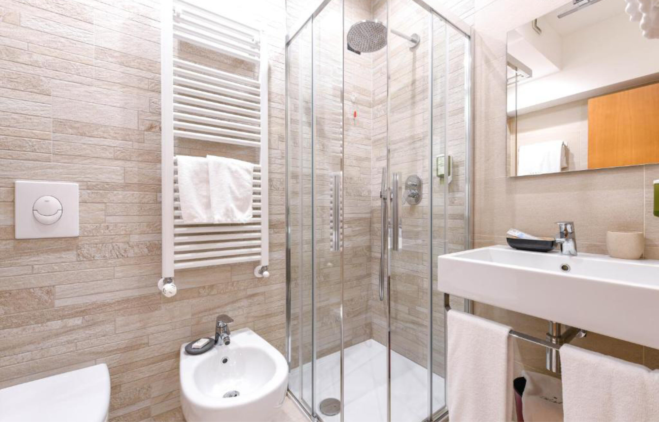 Kleines Badezimmer mit Duschkabine aus Glas, weißem Bidet, Handtuchheizkörper und Waschbecken mit Spiegel und oranger Wand im Hintergrund