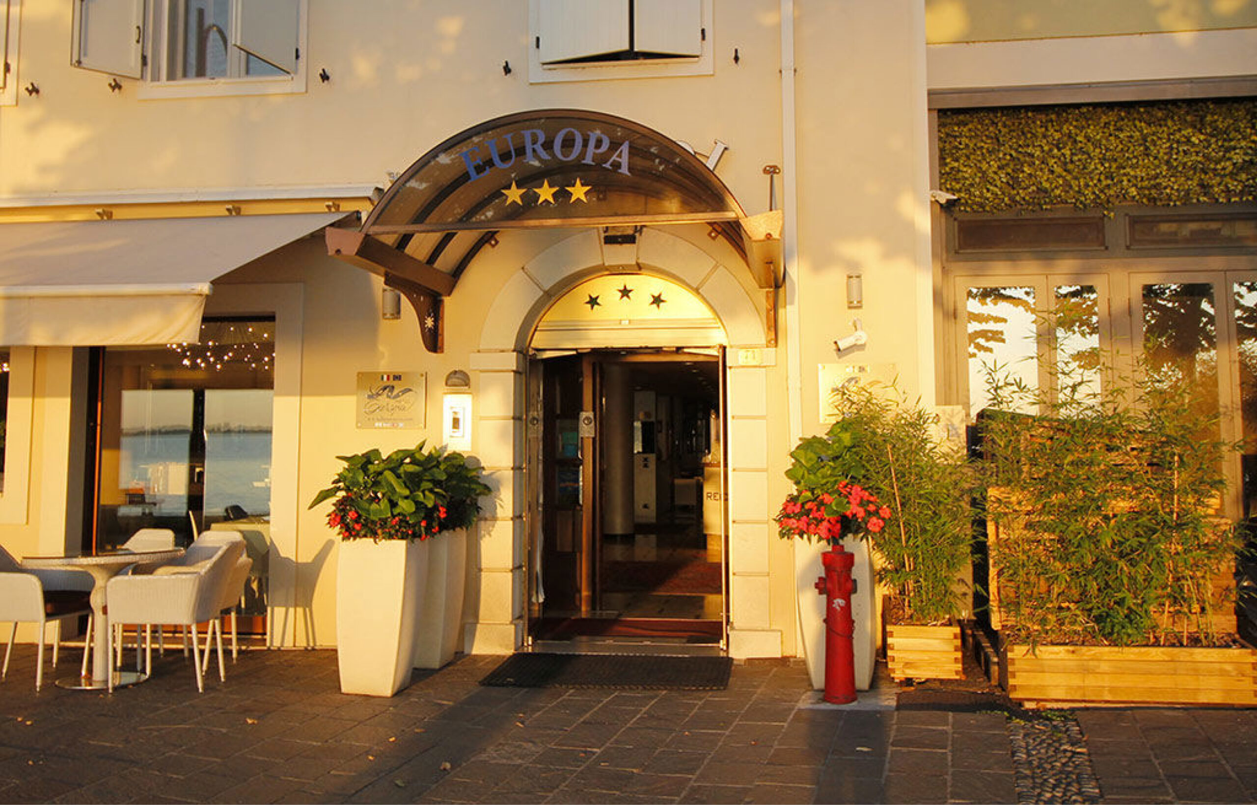 Eingang eines Hotels mit dem Schriftzug 'EUROPA' über dem Bogen und drei Sternen, flankiert von großen Pflanzkübeln und Sitzgelegenheiten im Außenbereich