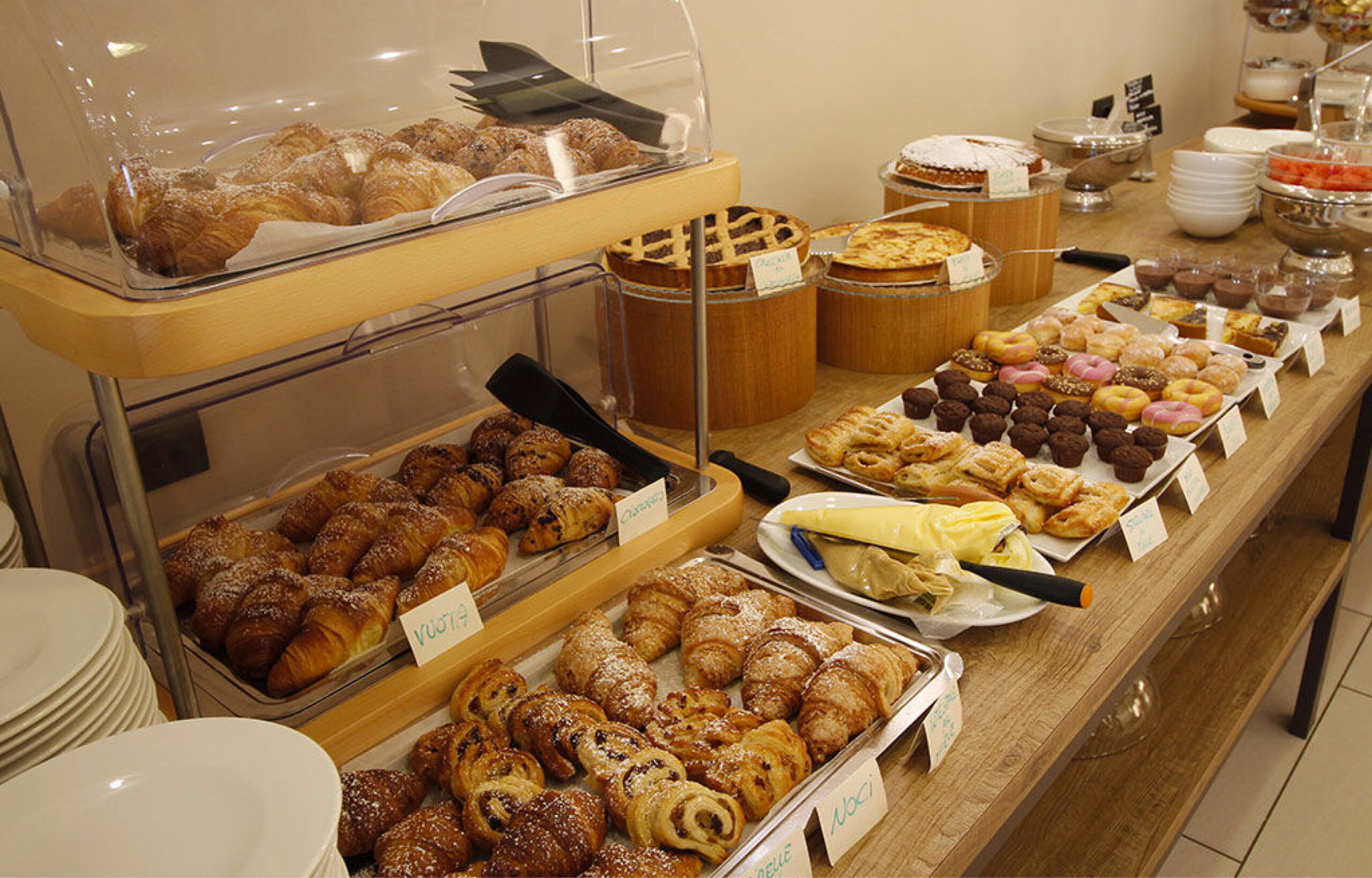 Buffet mit verschiedenen Backwaren wie Croissants, Donuts, Kuchen und Gebäck auf einem Holztisch