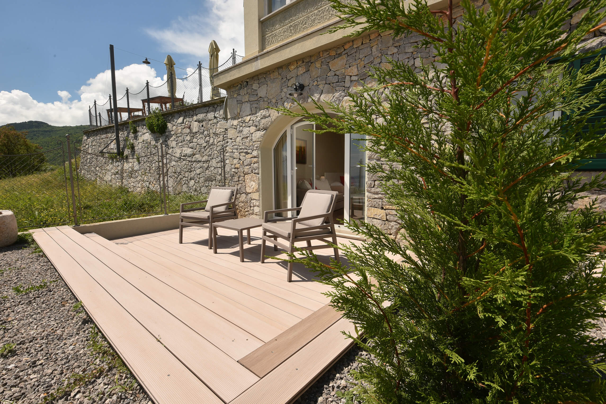 Terrasse mit zwei Stühlen vor einem Haus mit Steinmauer und Blick auf bewaldete Hügel im Hintergrund