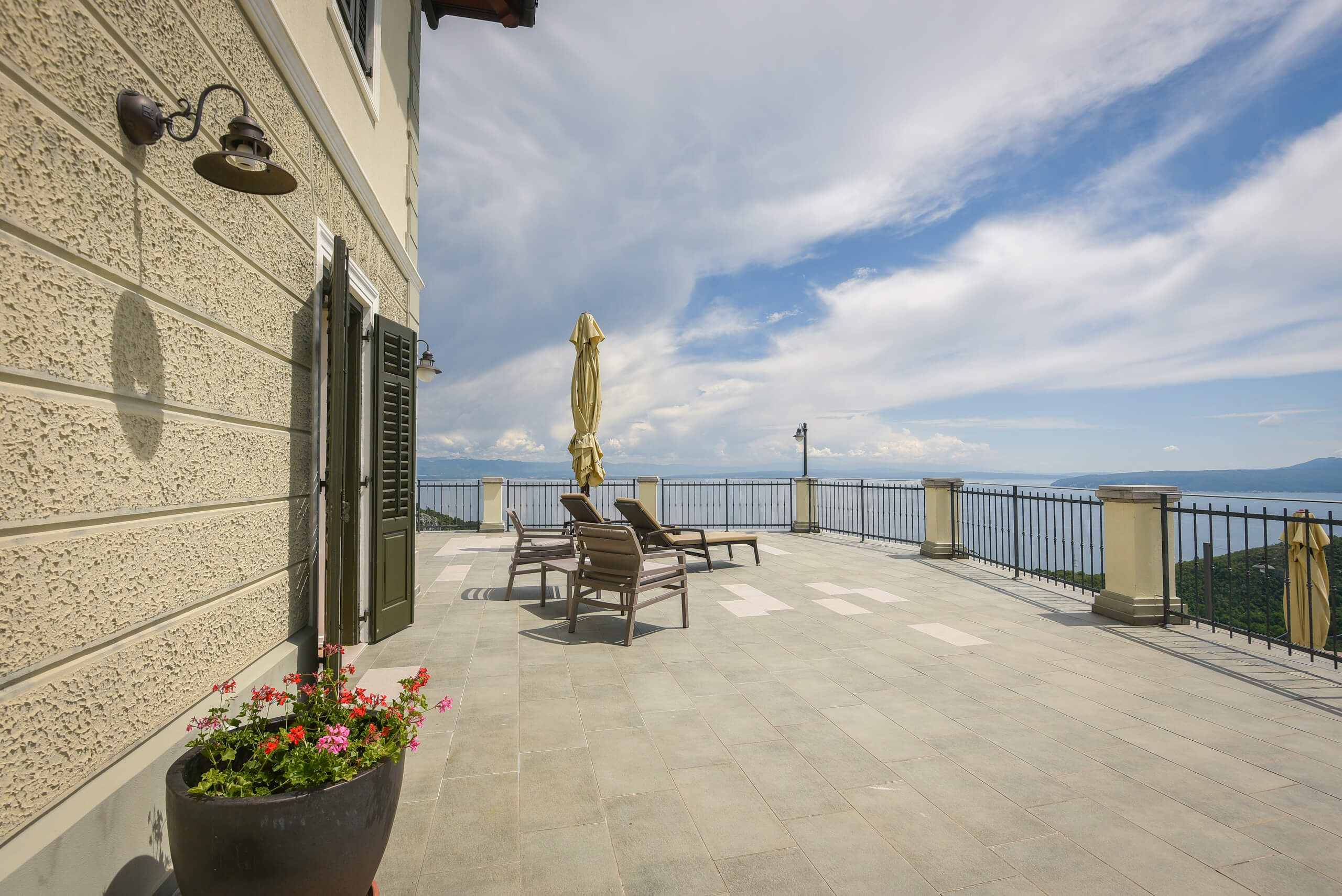 Terrasse mit Stühlen, geschlossenen Sonnenschirmen und Blumentopf an einem Gebäude mit Blick auf das Meer