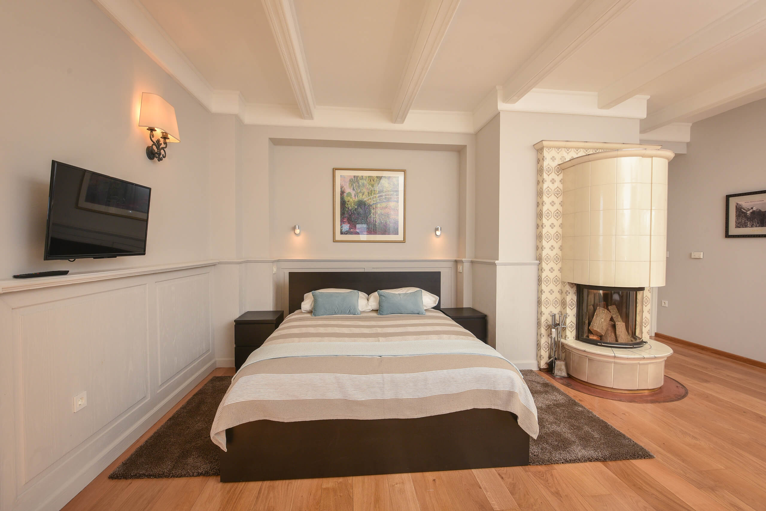 Schlafzimmer mit Doppelbett, Wandlampe, Fernseher an der Wand und rundem Kamin in einer Ecke